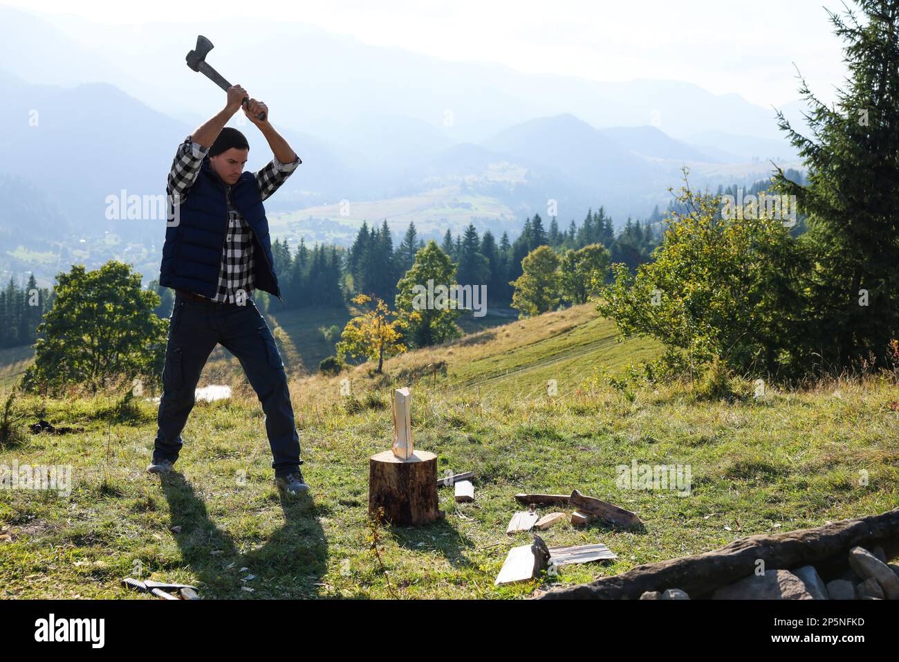 Ein gutaussehender Mann mit Axt, der auf dem Hügel Brennholz schneidet Stockfoto Ein gutaussehender Mann mit Axt, der auf dem Hügel Brennholz schneidet Stockfoto