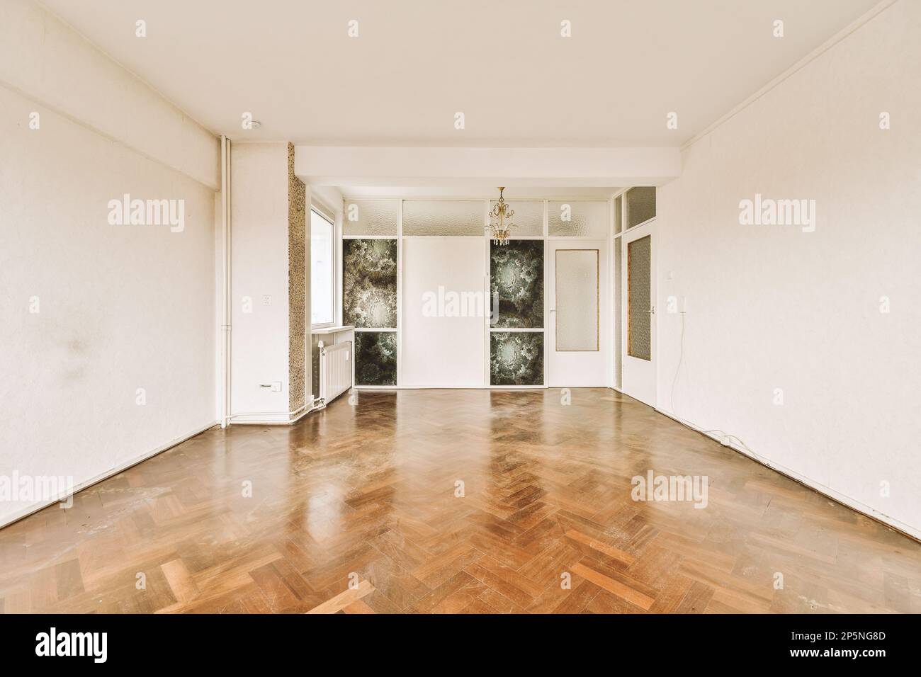 Ein leeres Wohnzimmer mit Holzfußboden und großen Fenstern mit Blick auf den Garten draußen, von innen genommen Stockfoto