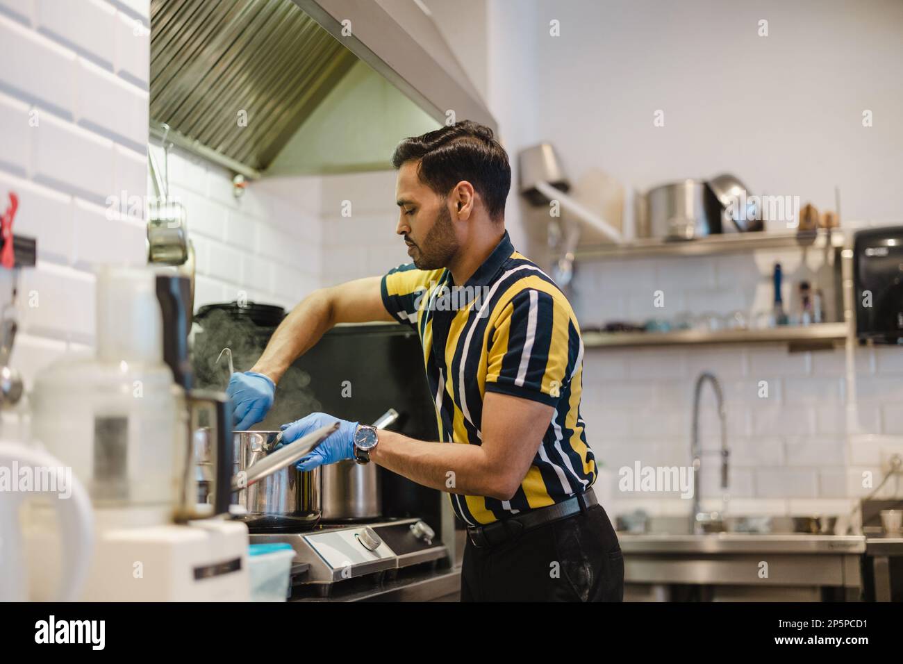 Junger Mann, der in der kommerziellen Küche frisches Essen zubereitet Stockfoto