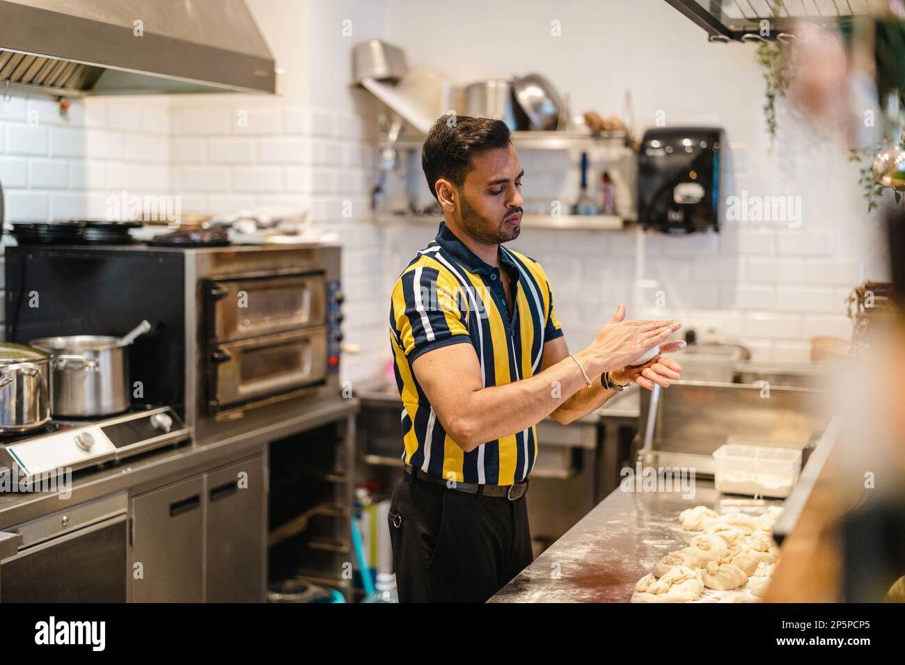 Junger Mann, der in der kommerziellen Küche frisches Essen zubereitet Stockfoto