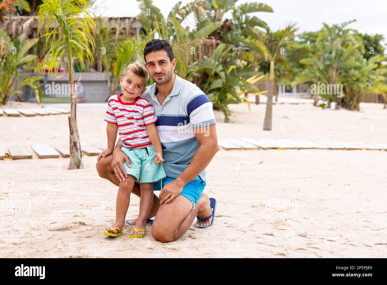 Porträt von glücklichen, birassischen Vater und Sohn, die sich am Strand umarmen und lächeln, in Zeitlupe Stockfoto