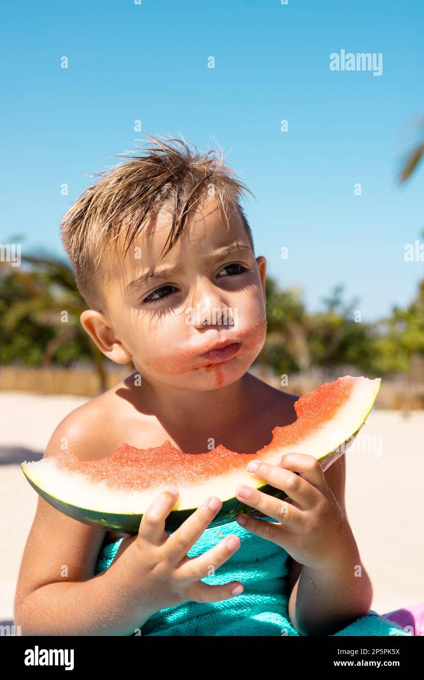 Ein glücklicher, birassistischer Junge, der Wassermelone am Pool isst Stockfoto