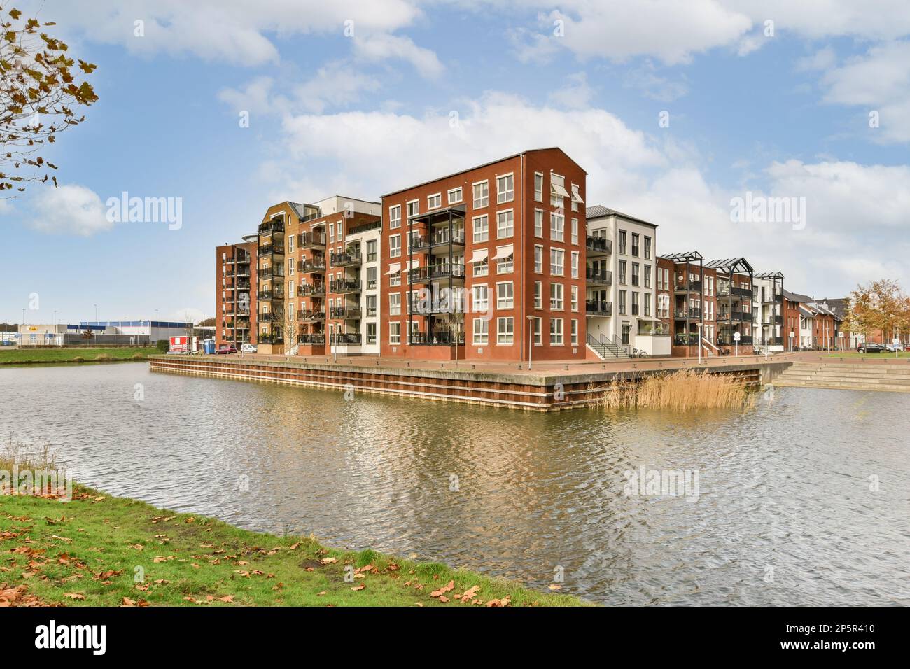 Amsterdam, Niederlande - 10. April 2021: Einige Gebäude an der Seite eines Wasserkörpers mit Bäumen und Blättern im Vordergrund - das Bild stammt von der anderen Seite des Flusses Stockfoto