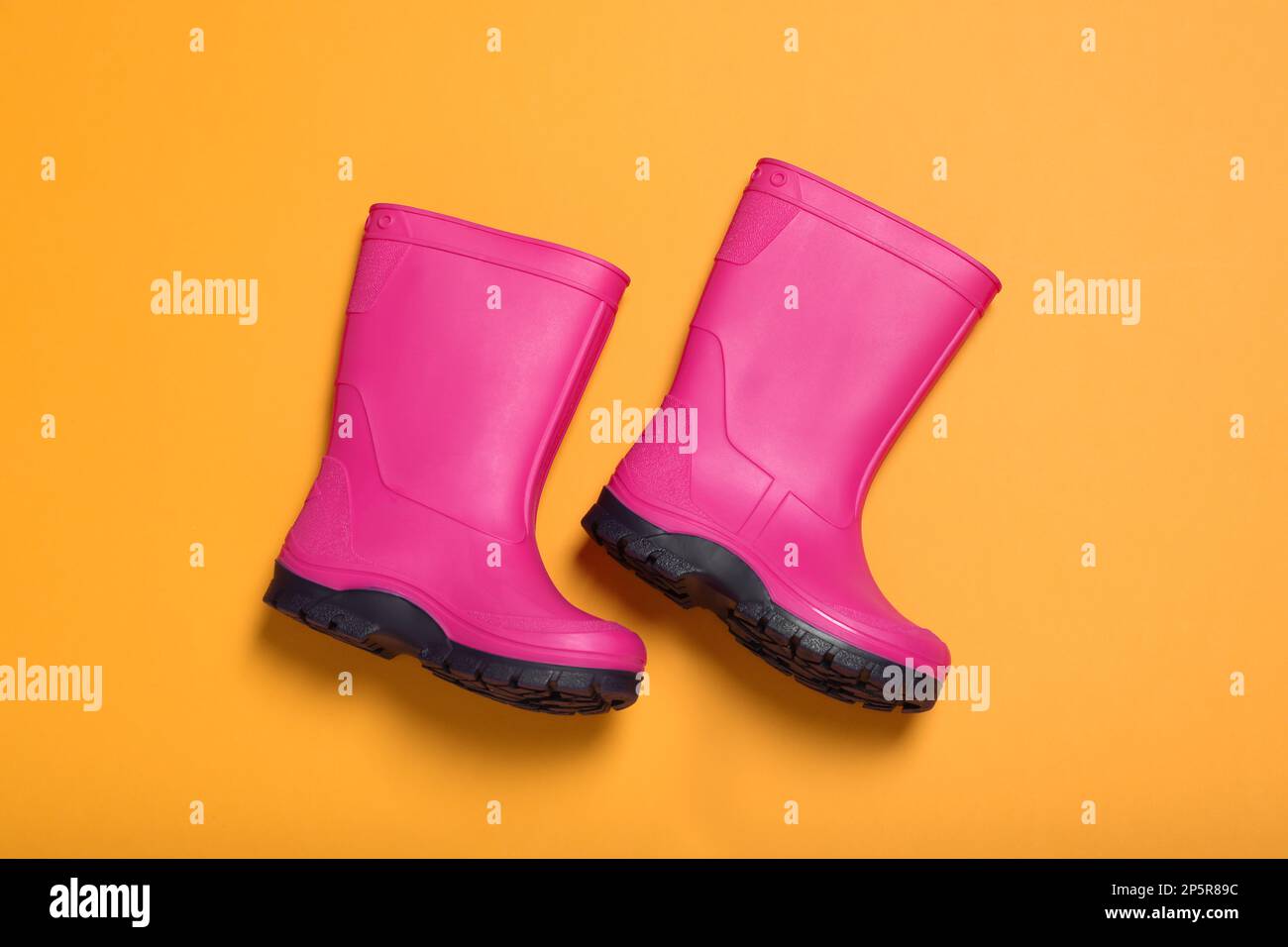 Ein Paar leuchtend pinkfarbene Gummistiefel auf orangefarbenem Hintergrund, Draufsicht Stockfoto