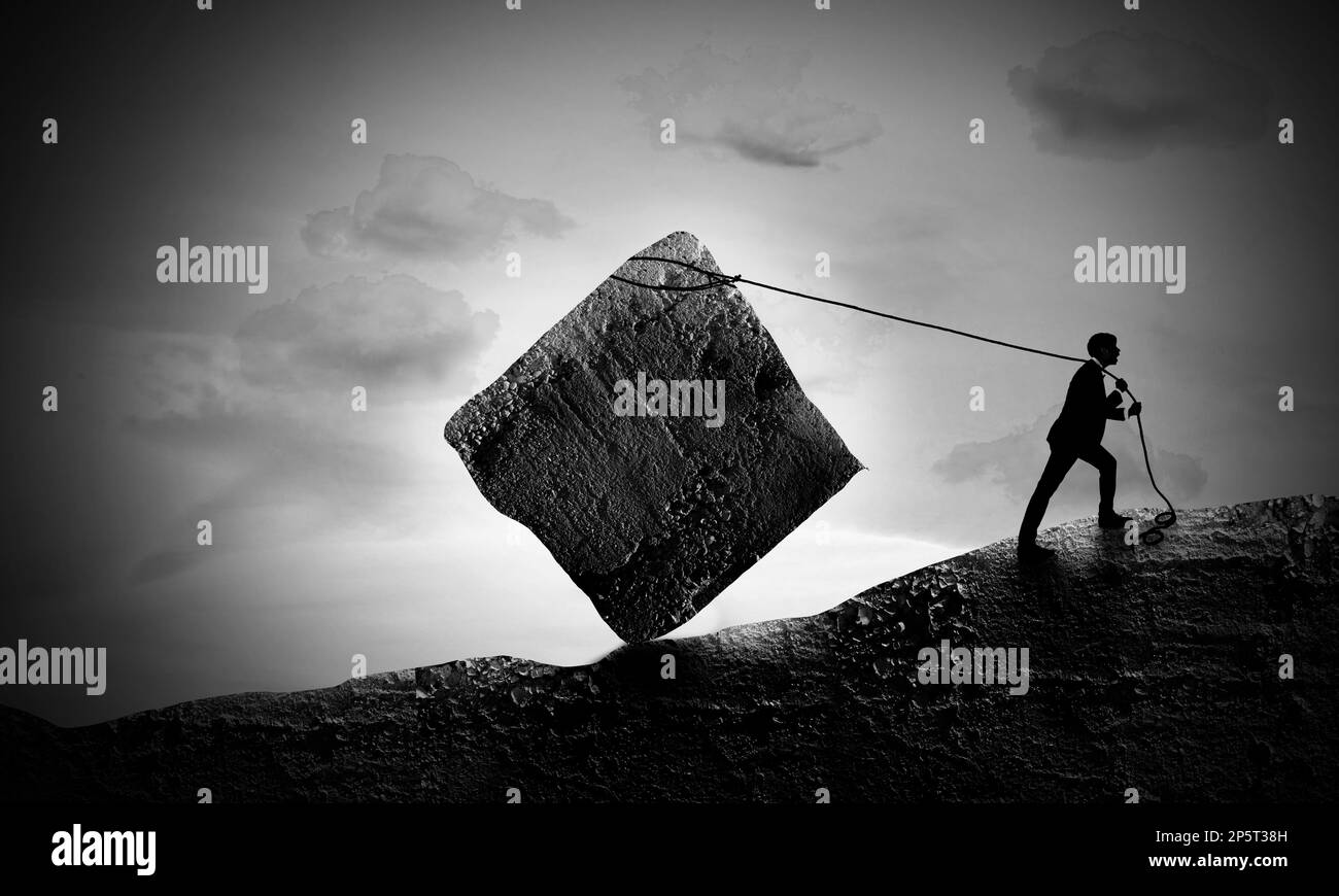 Eine surreale Szene, in der ein junger Geschäftsmann Einen Steinblock nach Hill zieht. Sisyphus-Konzept. Der erschöpfte Mann zieht kaum den Kampf. Stockfoto