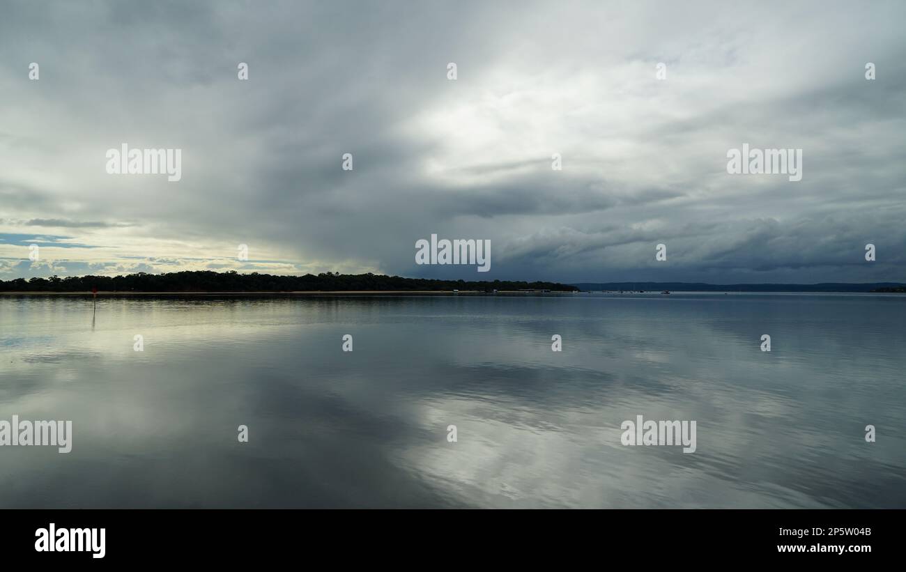 Am Vormittag strahlt Licht durch den wolkigen Himmel, reflektiert auf dem ruhigen Wasser der Moreton Bay zwischen Victoria Point und Coochiemudlo Island Stockfoto