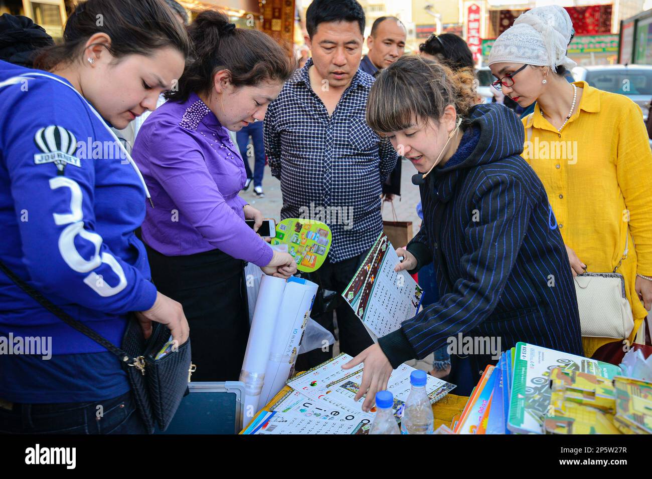 Händler, die Hausaufgaben-Übungsbücher für Kinder und eine Menge Zuschauer auf dem traditionellen Markt unter freiem Himmel in Urumqi, Xinjiang, China, verkaufen Stockfoto