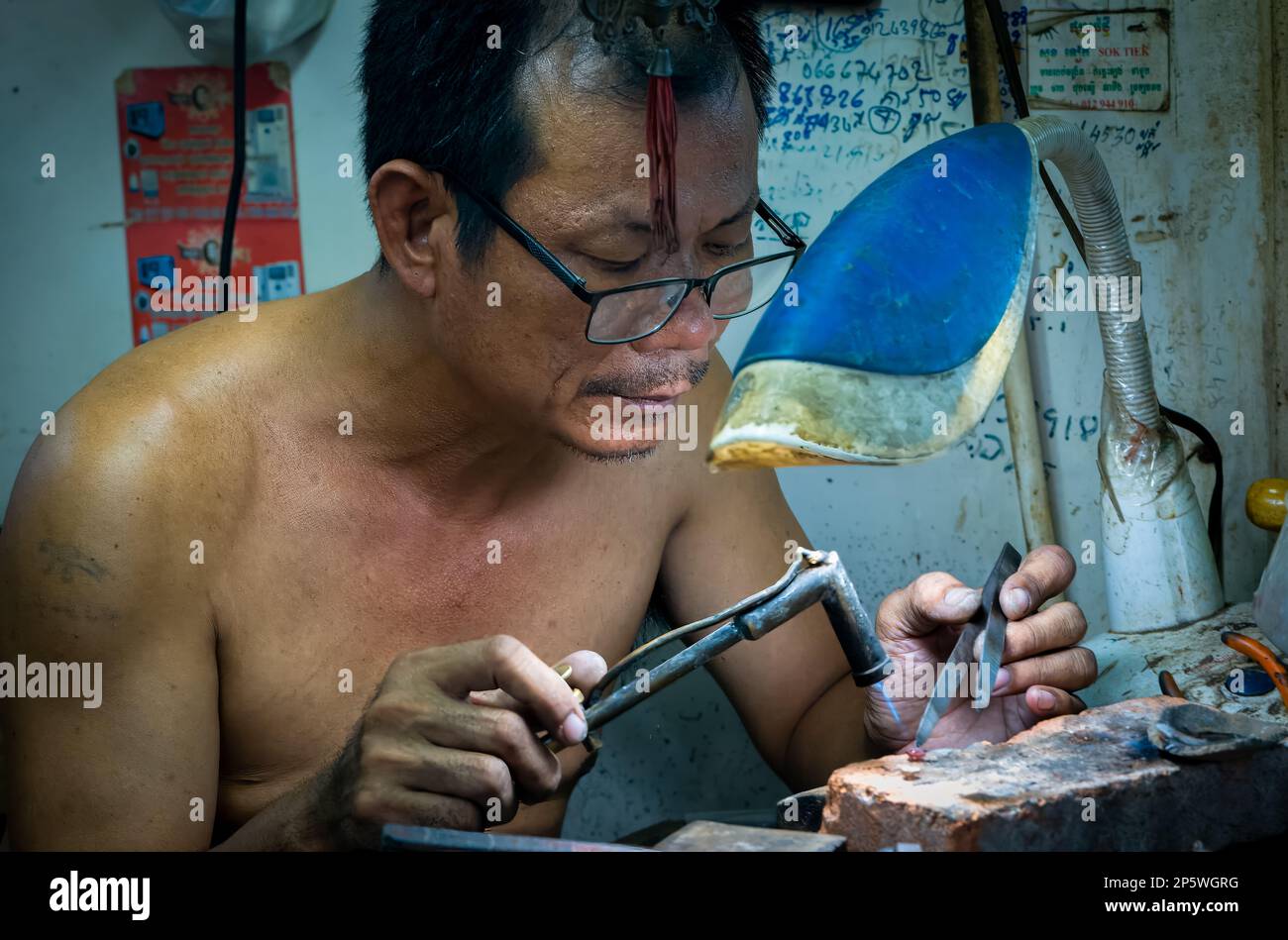 Ein Juwelier und Goldschmied arbeitet an einem Goldstück mit einer Lötlampe und Pinzette im Central Market in Phnom Penh, Kambodscha. Stockfoto