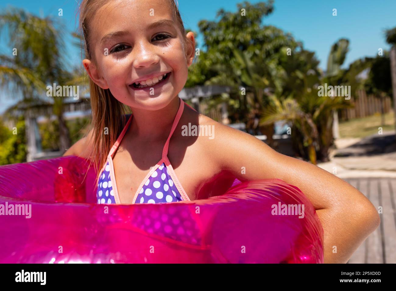Porträt eines fröhlichen, birassischen Mädchens, das lächelt und einen Schwimmring am Pool hält Stockfoto