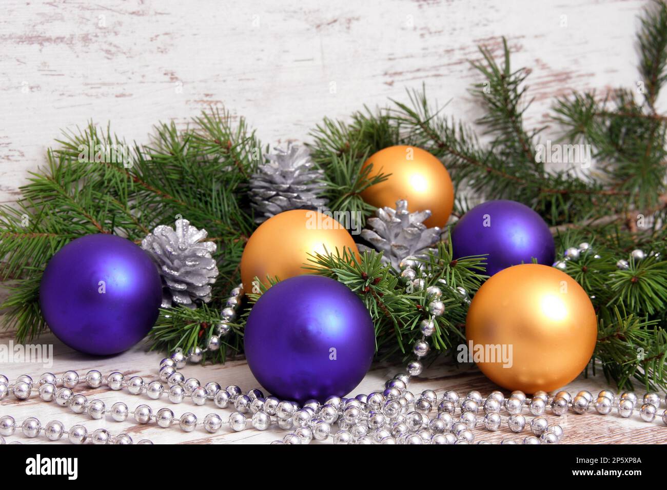 Weihnachtsdekoration mit violetten und goldenen Kugeln, Fichtenzweigen, Kiefernzapfen und Silberkette Stockfoto