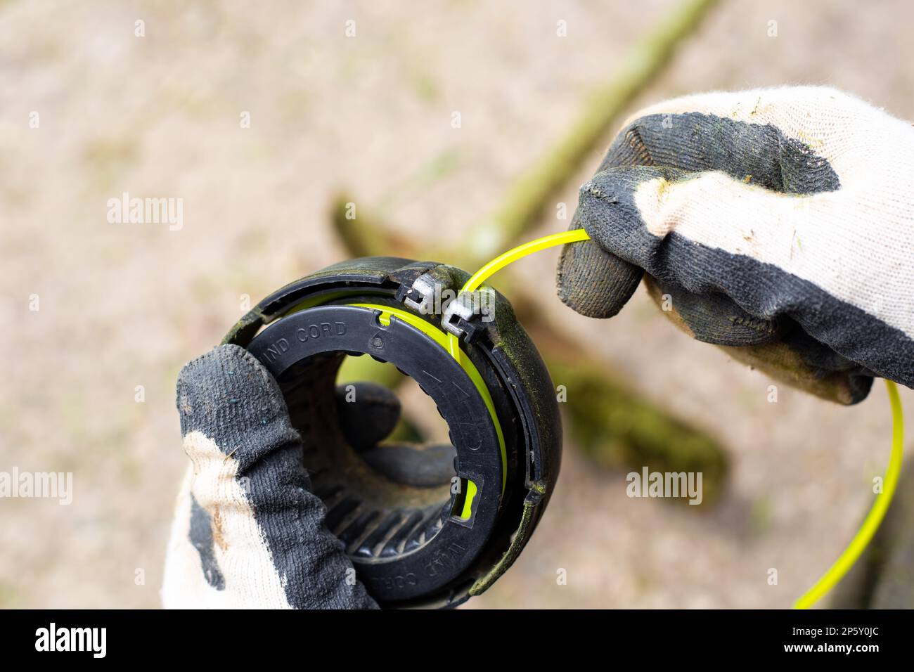 Ein Mann fädelt eine Leine, um Gras in die Spule eines Benzinmähers zu schneiden. Stockfoto