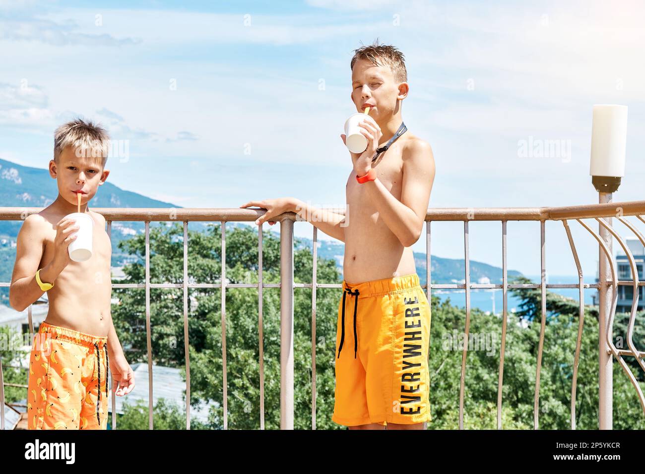 Geschwister im Vorschulalter und Schuljungen trinken Cocktails auf der Hotelterrasse. Brüder in kurzen Hosen genießen Sommerferien im Wasserpark an sonnigen Tagen Stockfoto