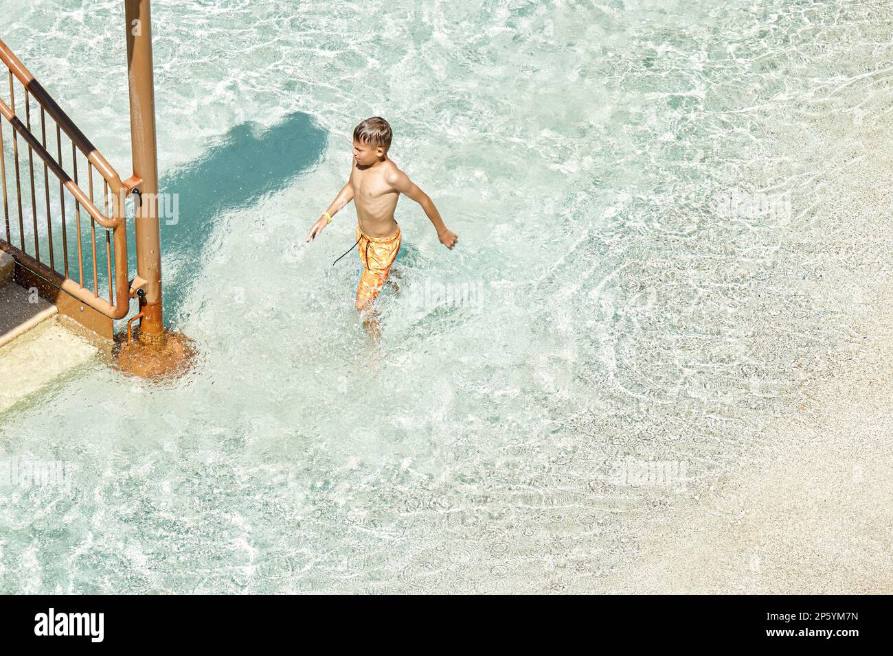 Der Schuljunge verlässt den Swimmingpool mit klarem blauem Wasser an sonnigen Tagen. Der blonde Junge genießt im Sommerurlaub im Aqua Park lustige Aktivitäten Stockfoto