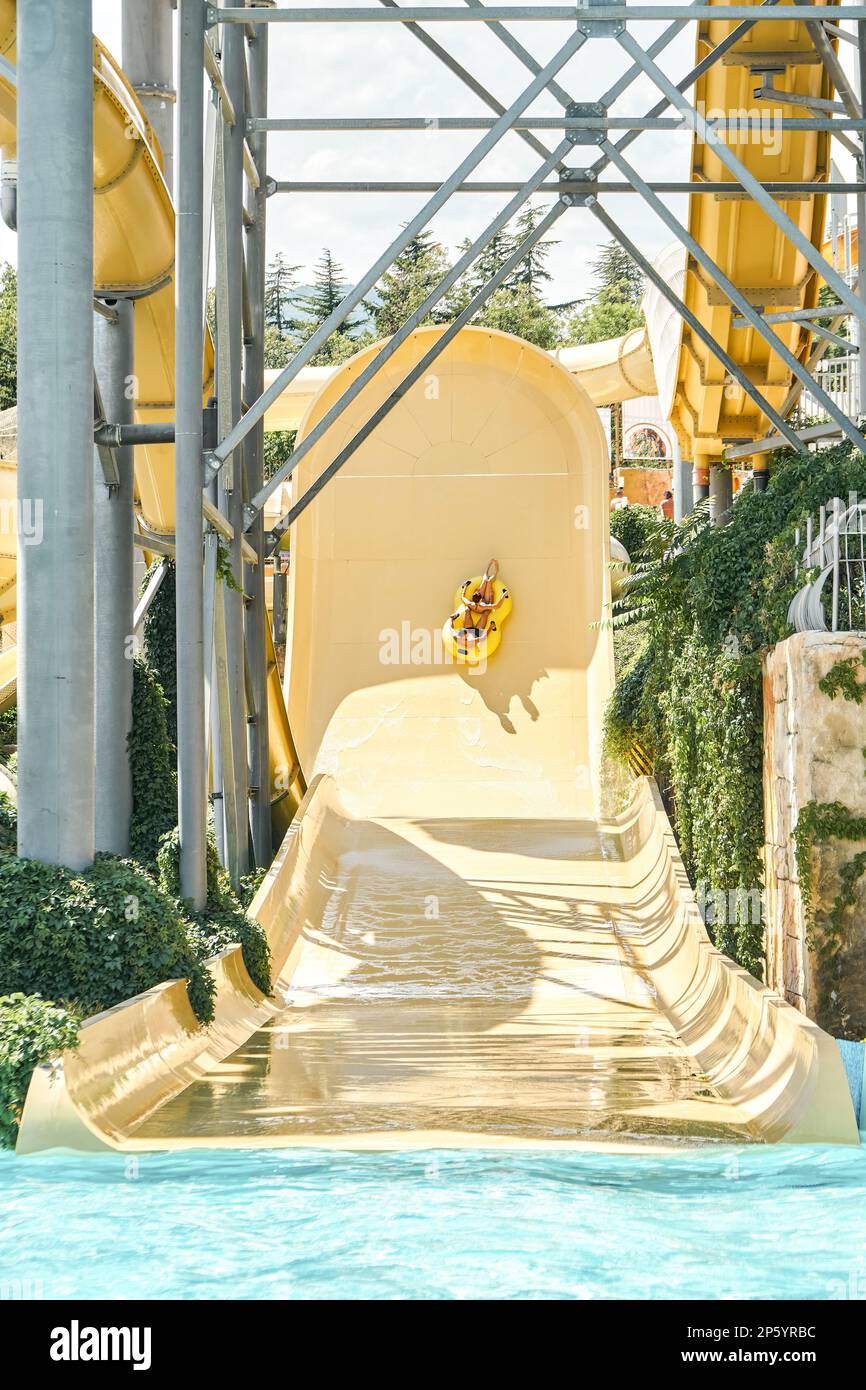 Die Leute fahren auf einer großen Rutsche und fallen in den Swimmingpool mit sauberem blauem Wasser. Touristen genießen unterhaltsame Aktivitäten und Unterhaltung im beliebten Wasserpark Stockfoto