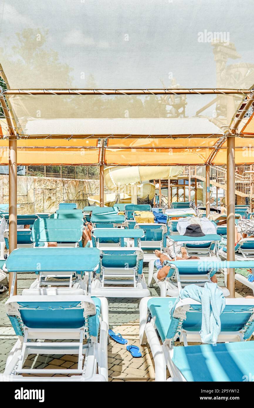 Blaue Sonnenliegen in Reihen unter transparentem Baldachin. Sonnenschutz über den Liegestühlen in der Nähe des Swimmingpools im touristischen Wasserpark Stockfoto