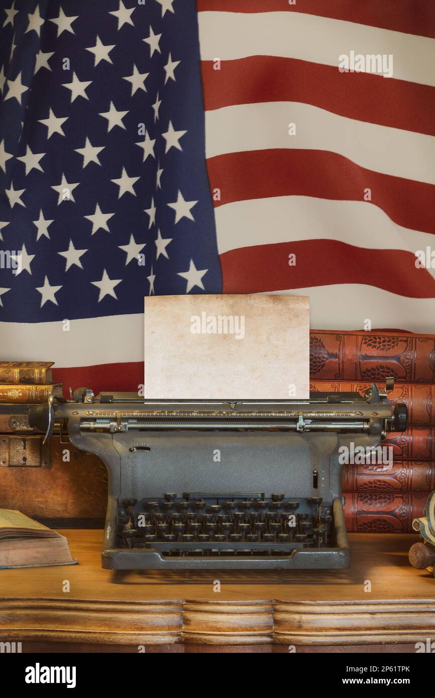 Ein alter Holzschreibtisch mit einer alten Schreibmaschine, die ein leeres Blatt Papier vor der US-Flagge hält Stockfoto