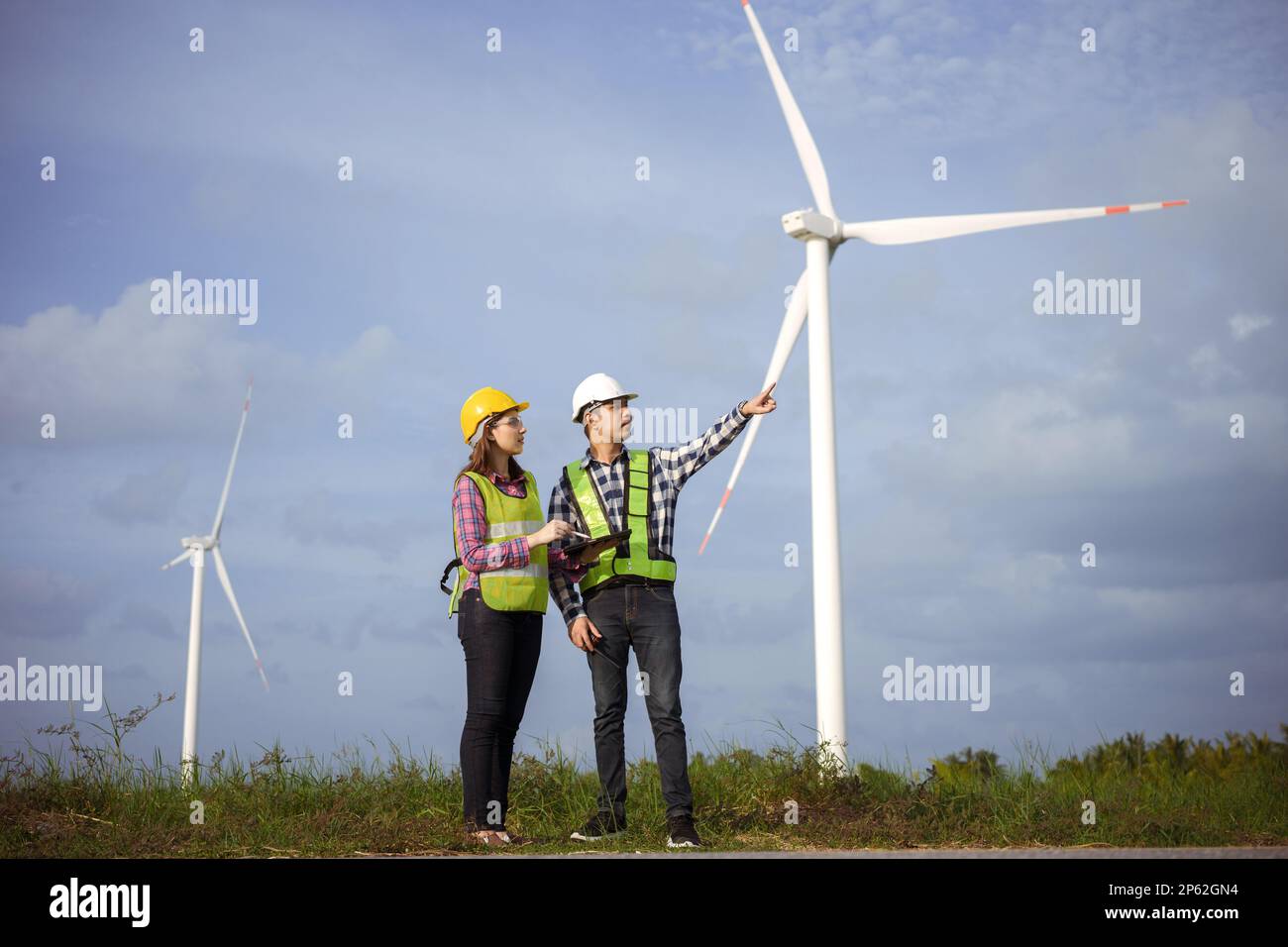 Team asiatischer Ingenieure, die das Windturbinenfeld besprechen und den Fortschritt prüfen. Stockfoto