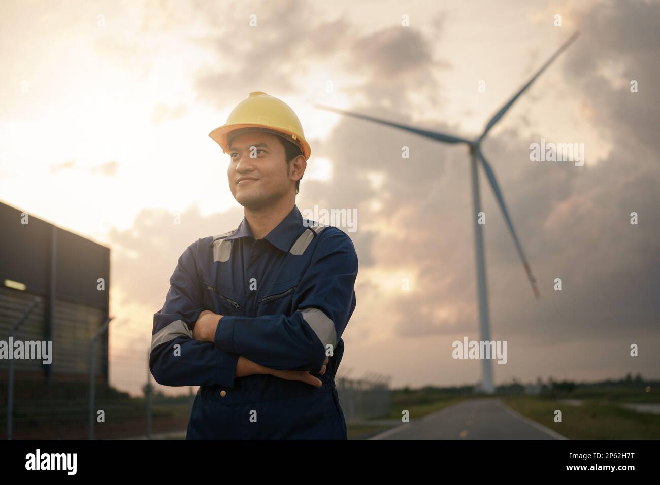 Glücklicher junger Ingenieur in Uniform, der auf dem Feld der Windkraftanlage steht. Stockfoto