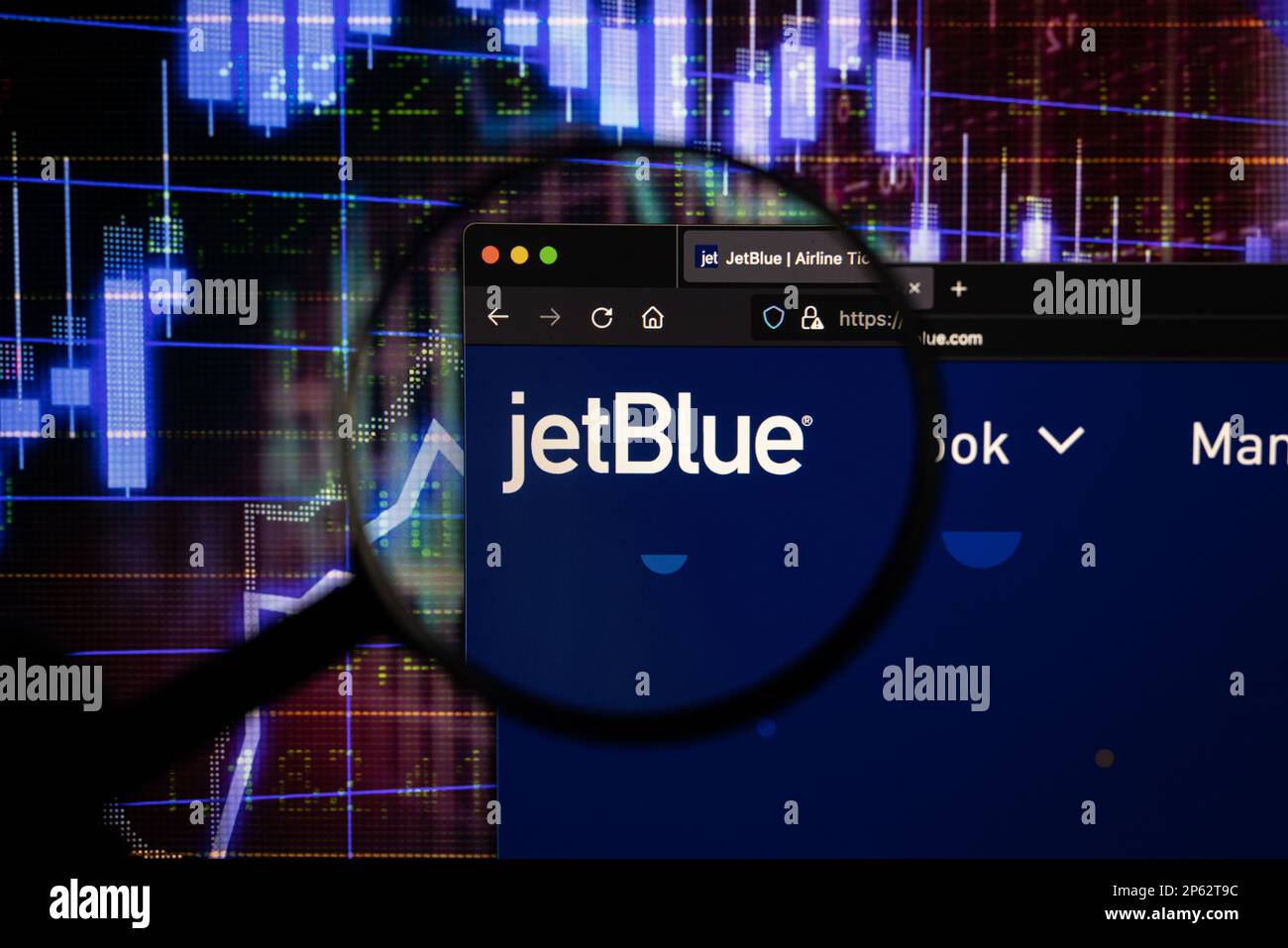 Firmenlogo der Fluggesellschaft JetBlue auf einer Website mit verschwommenen Aktienmarktentwicklungen im Hintergrund, auf einem Bildschirm durch eine Lupe zu sehen Stockfoto