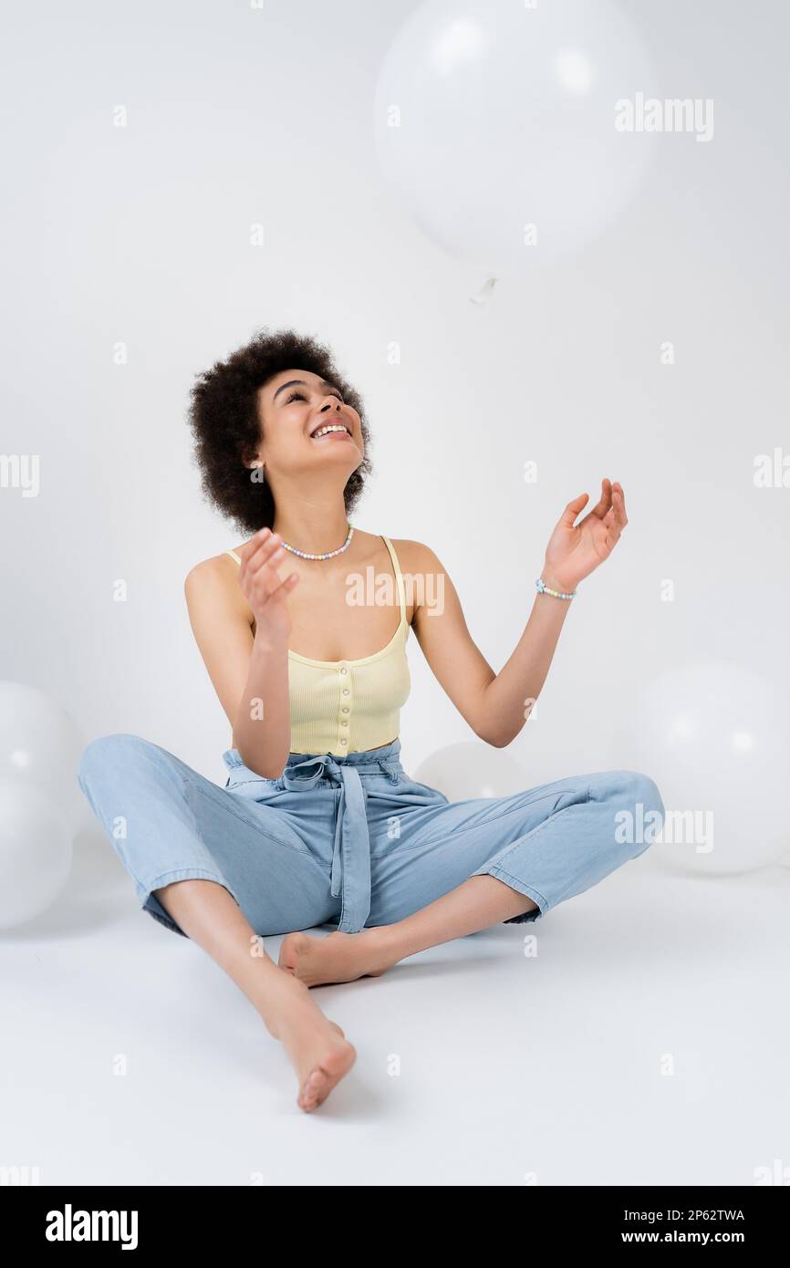 Positive afroamerikanische Frau wirft Ballon auf grauen Hintergrund, Börsenbild Stockfoto