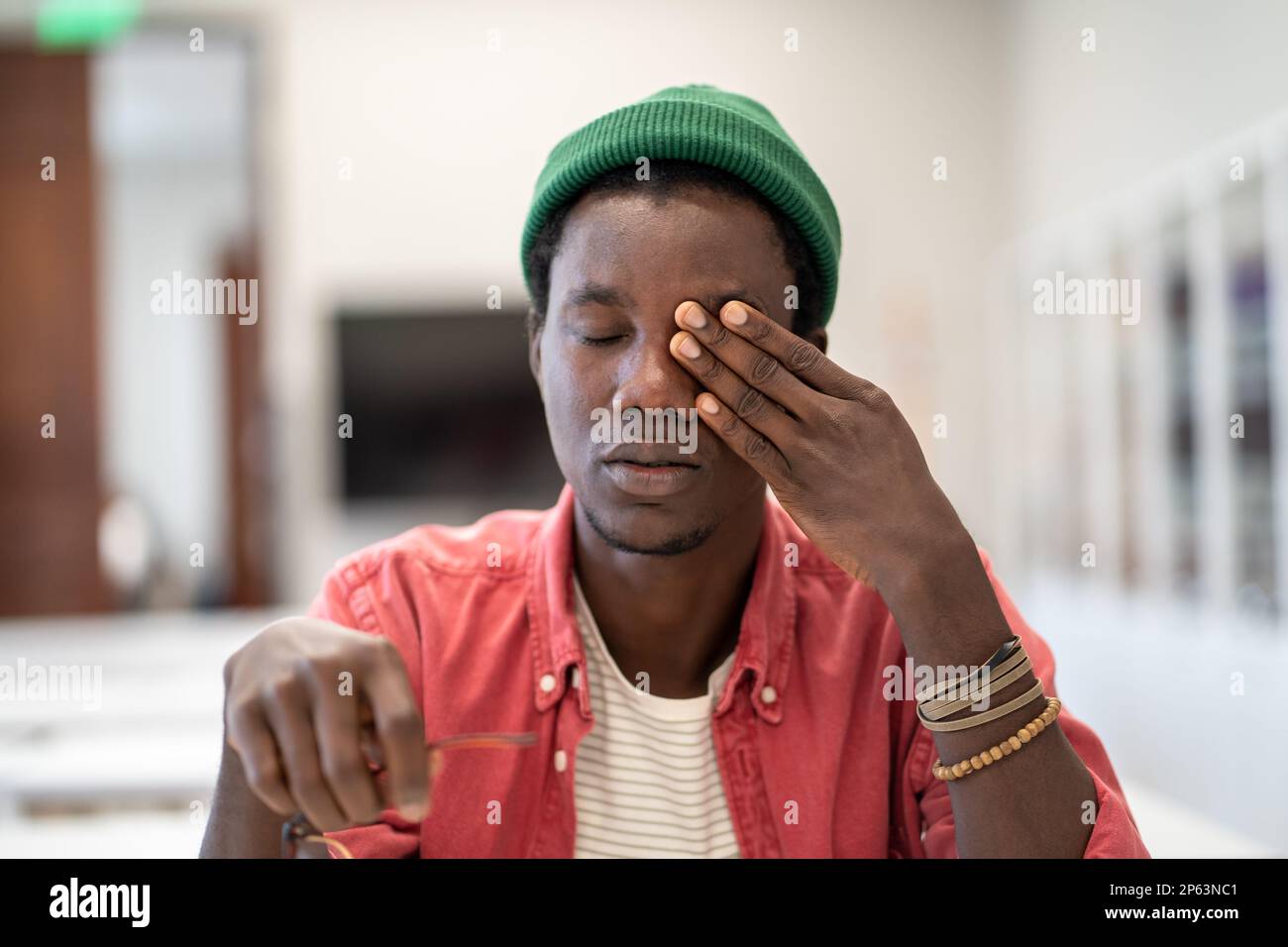 Ein müder, gestresster afrikanischer Student, der in der Bibliothek sitzt und die Augen massiert und sich unmotiviert fühlt, zu lernen Stockfoto