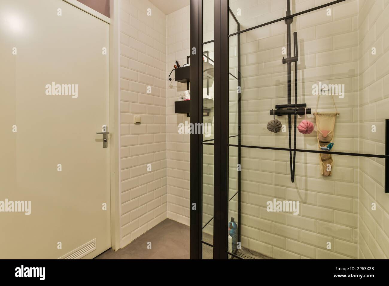 Ein Badezimmer mit weißen Fliesen an den Wänden und schwarzen Zierleisten um die Duschtür, die an der Wand befestigt ist Stockfoto