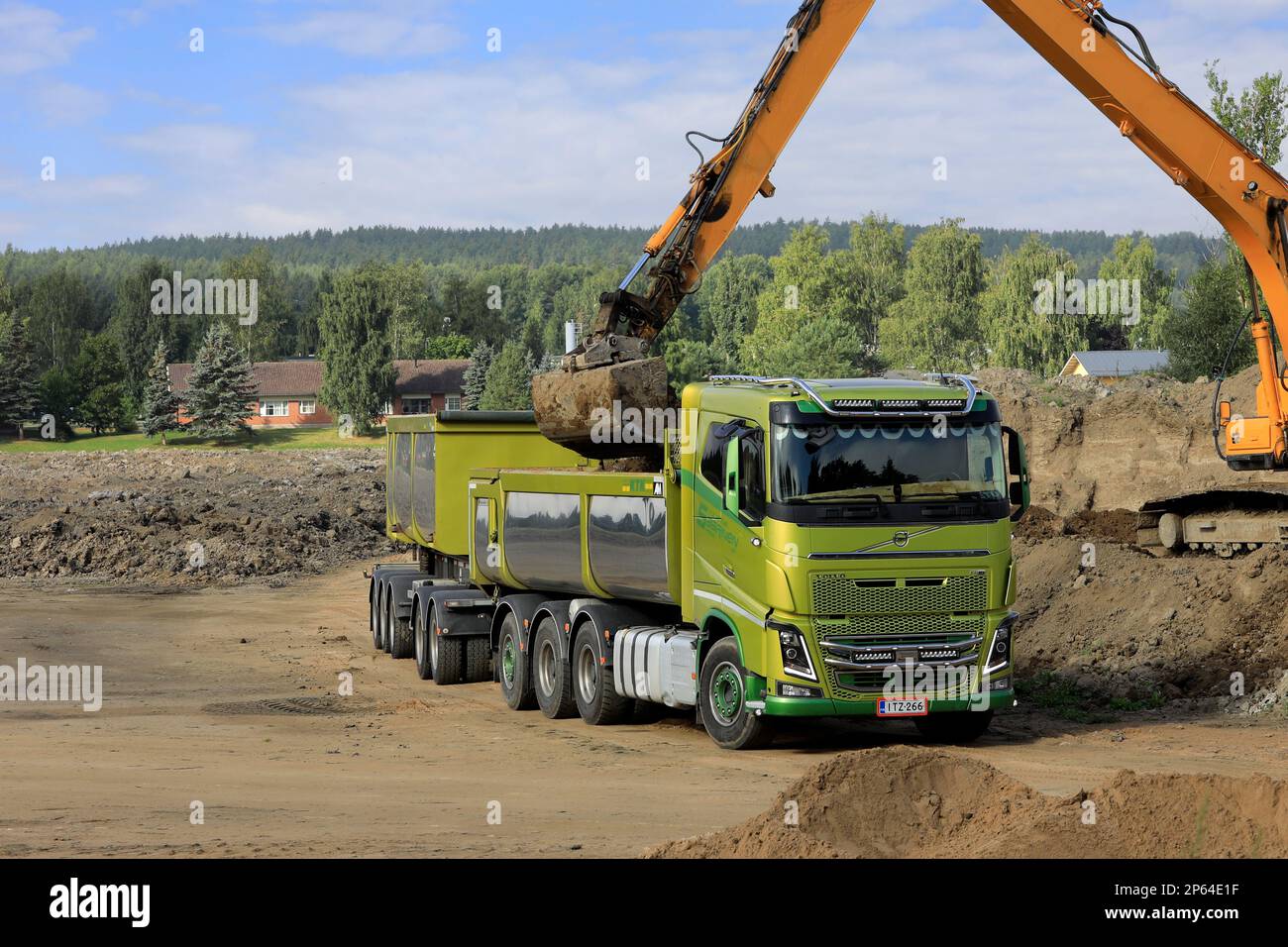 Raupenbagger lädt Erde an einem Sommertag auf den grünen Volvo FH16 Lkw-Kassettenwagen. Verbleibender Speicherplatz kopieren. Salo, Finnland. 27. August 2022. Stockfoto