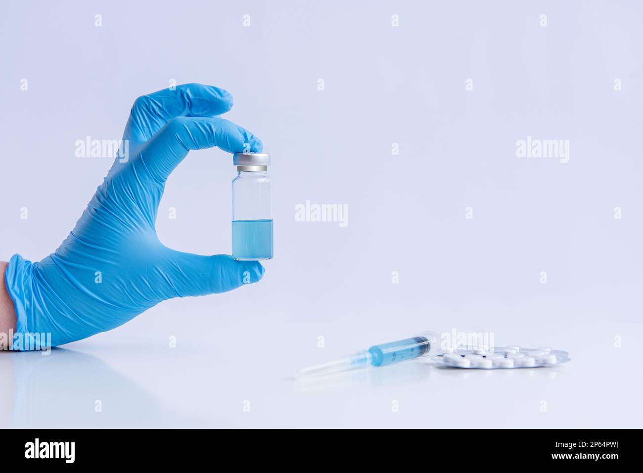Auf weißem isoliertem Hintergrund halten die Hände des Arztes in medizinischen blauen Handschuhen eine Ampulle Impfstoff gegen Virus Coronovirus. Spritze mit Gegenmittel, Schmerztabletten Stockfoto