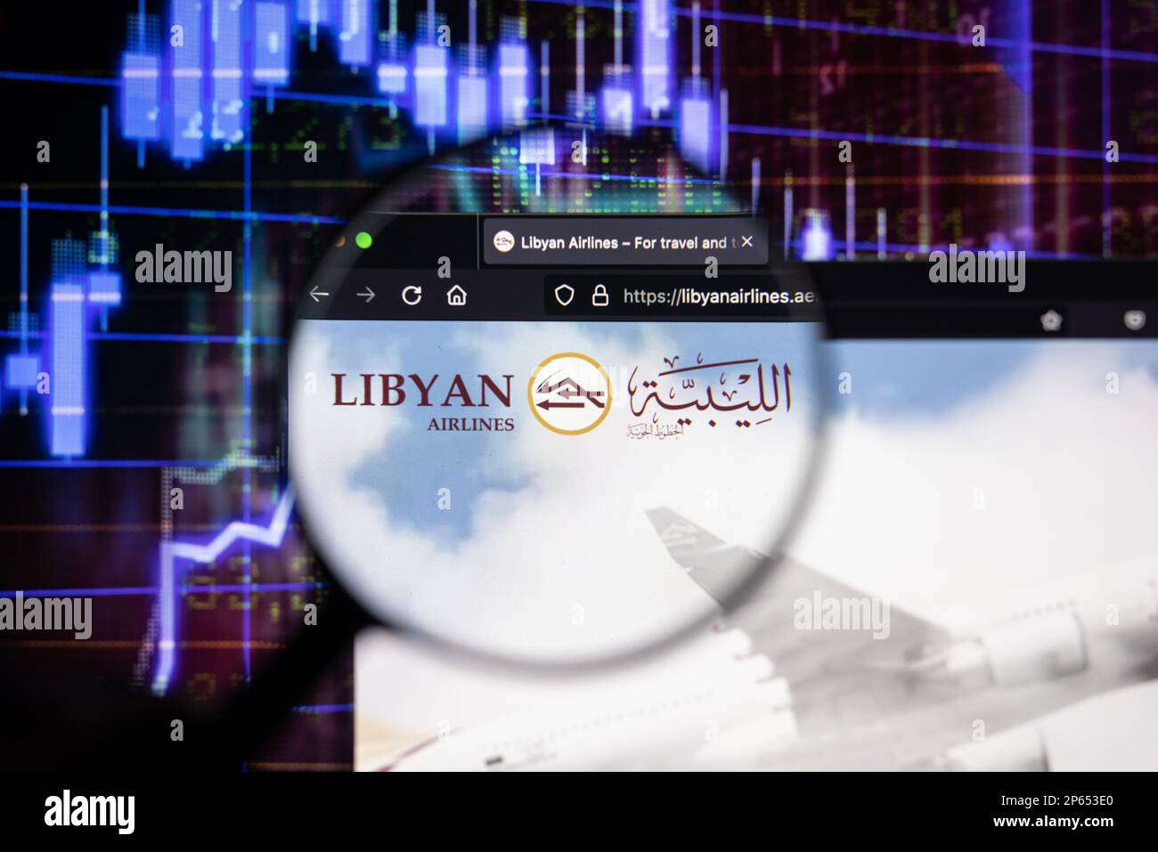 Firmenlogo von Lybian Ariways auf einer Website mit verschwommenen Aktienmarktentwicklungen im Hintergrund, auf einem Computerbildschirm durch eine Lupe zu sehen Stockfoto