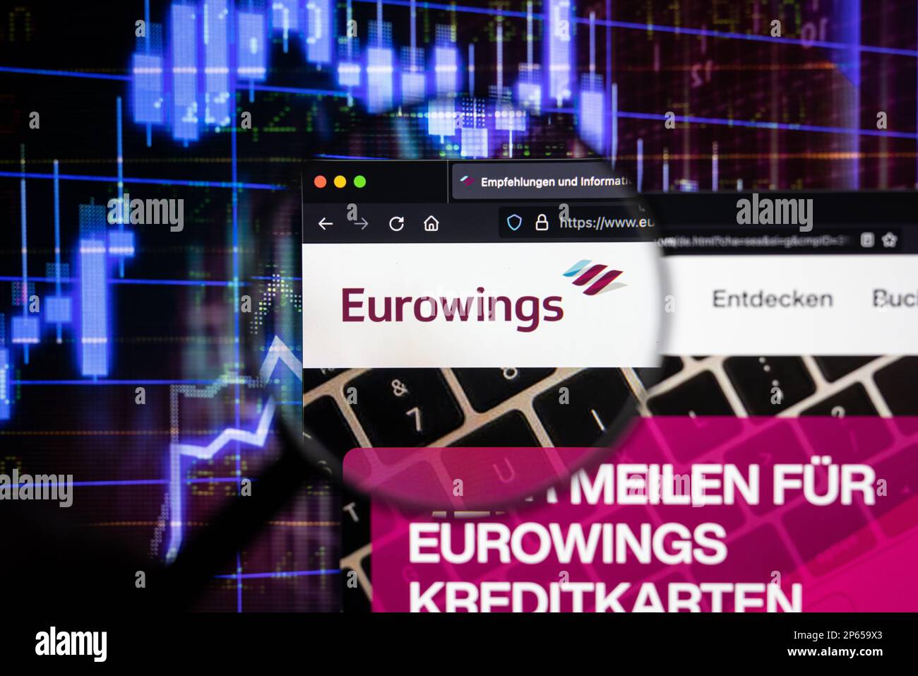 Logo der Fluggesellschaft Eurowings auf einer Website mit verschwommenen Entwicklungen am Aktienmarkt im Hintergrund, auf einem Bildschirm durch eine Lupe zu sehen Stockfoto