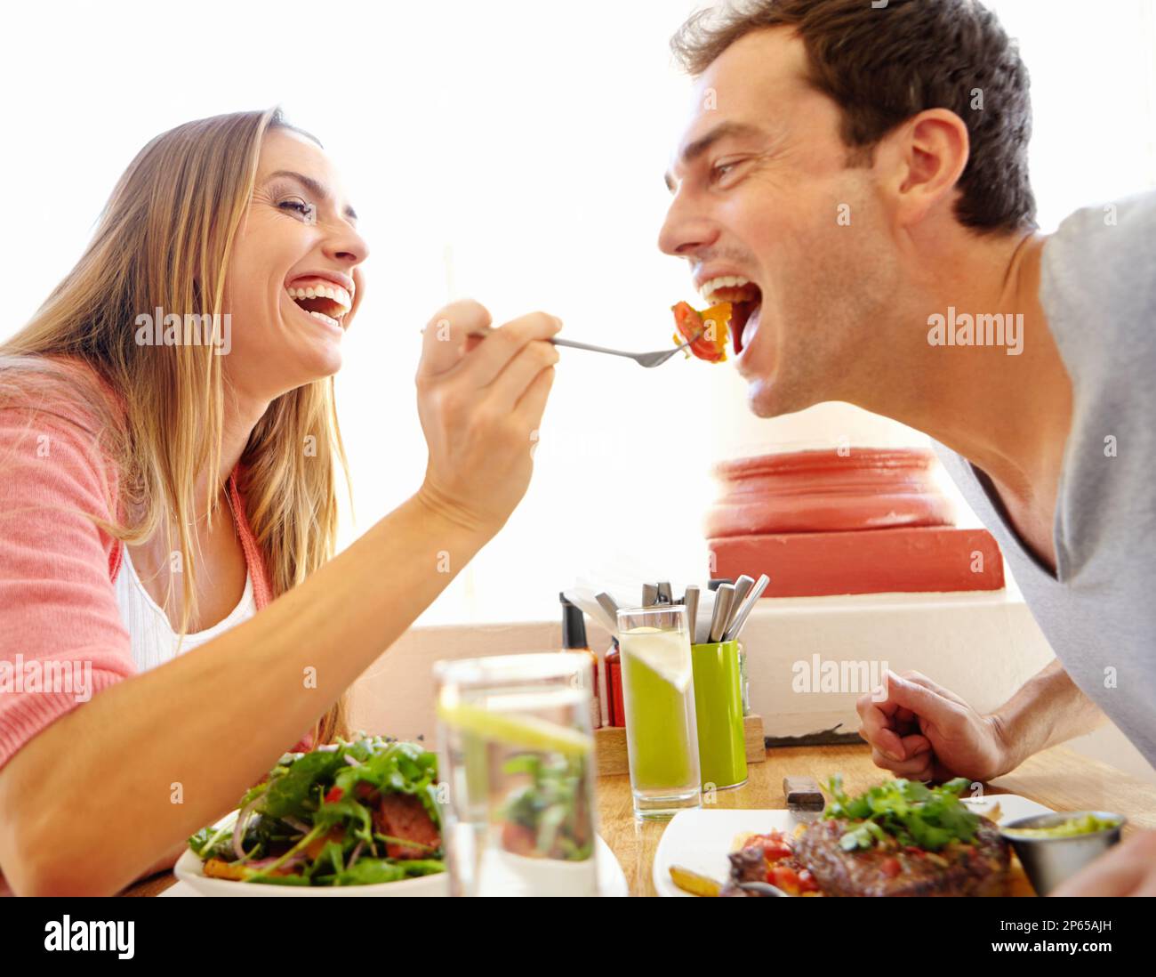 Das Geschmackserlebnis teilen. Eine glückliche junge Frau, die ihrem Freund einen Happen ihres Essens in einem Restaurant anbietet. Stockfoto