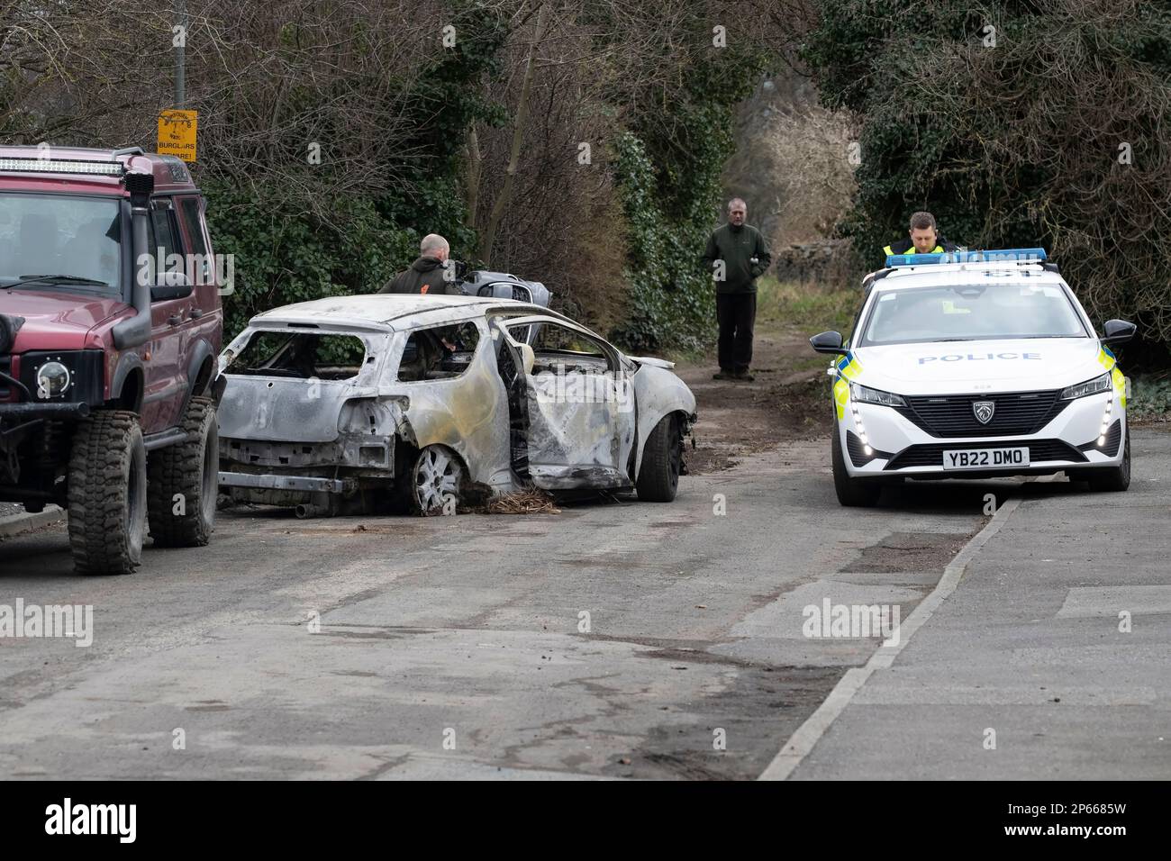 Polizeiauto und Geländefahrzeug am Tatort eines abgefackelten Wagens, das in einer Sackgasse in West Yorkshire aufgegeben wurde Stockfoto