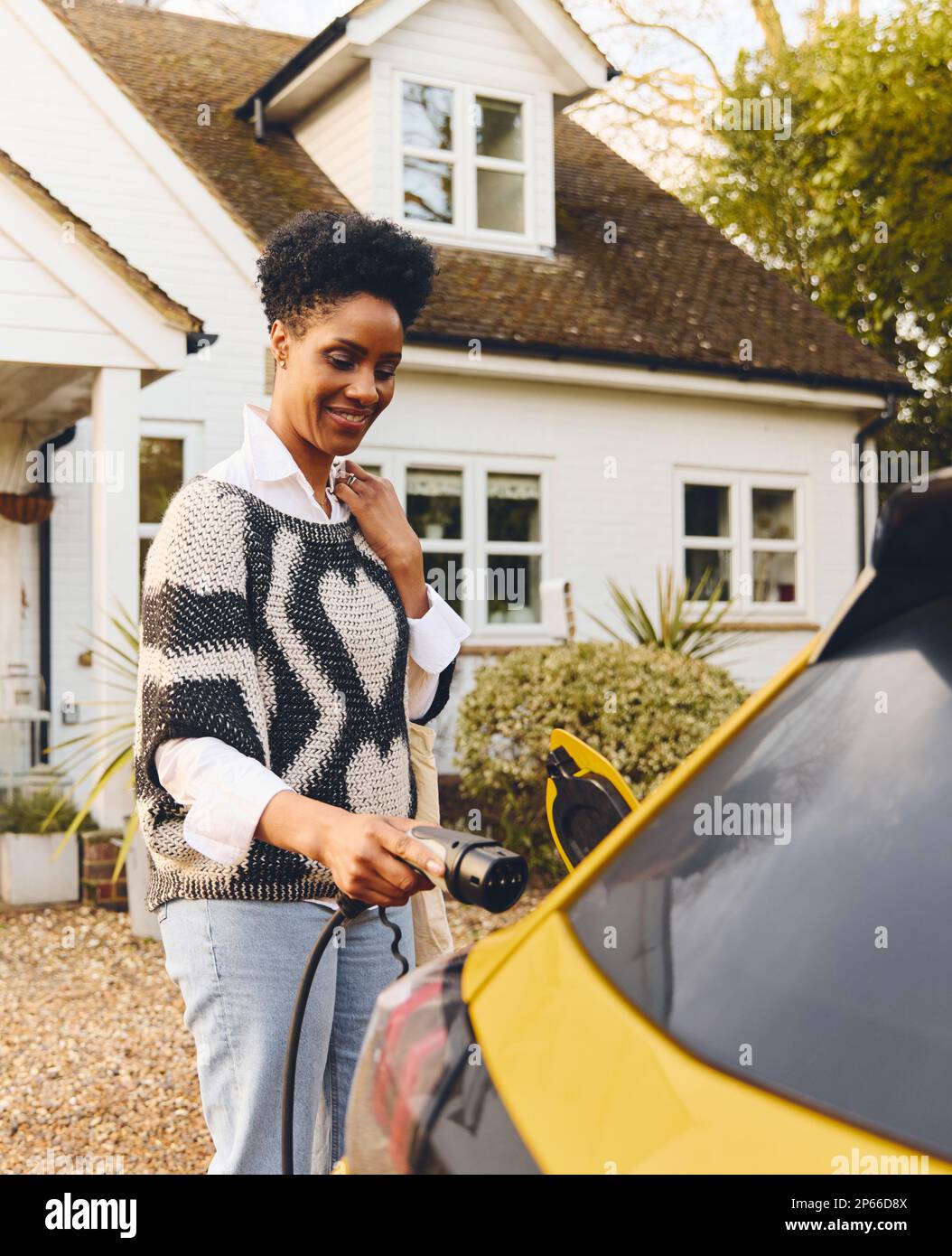 Eine Frau lädt ein Elektroauto auf der Auffahrt vor dem Haus auf Stockfoto