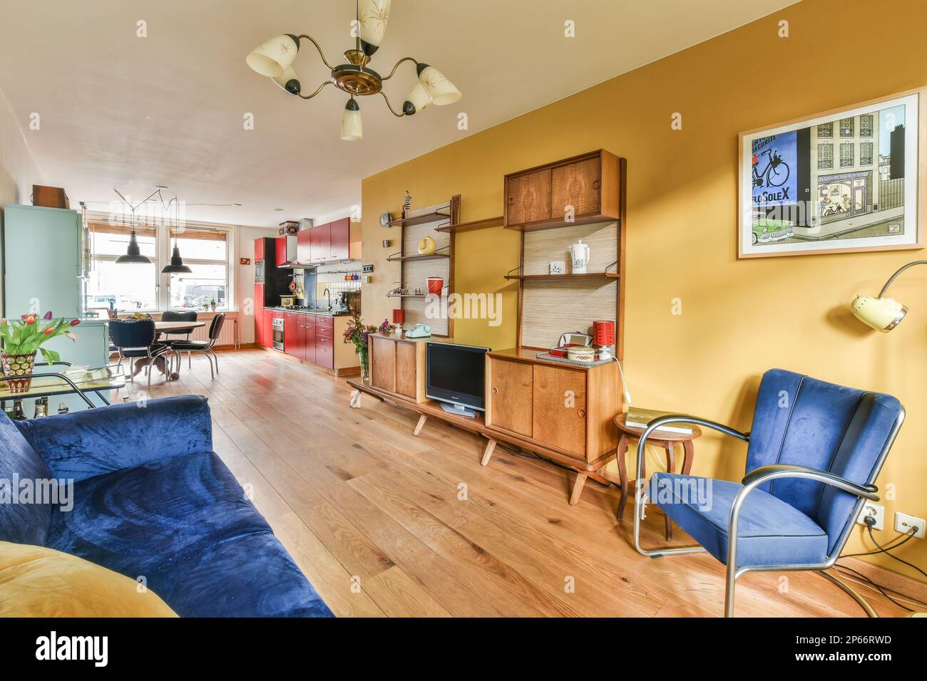 Ein Wohnzimmer mit gelben Wänden und blauen Sofas in der Mitte des Zimmers ist ein offener Küchenbereich Stockfoto