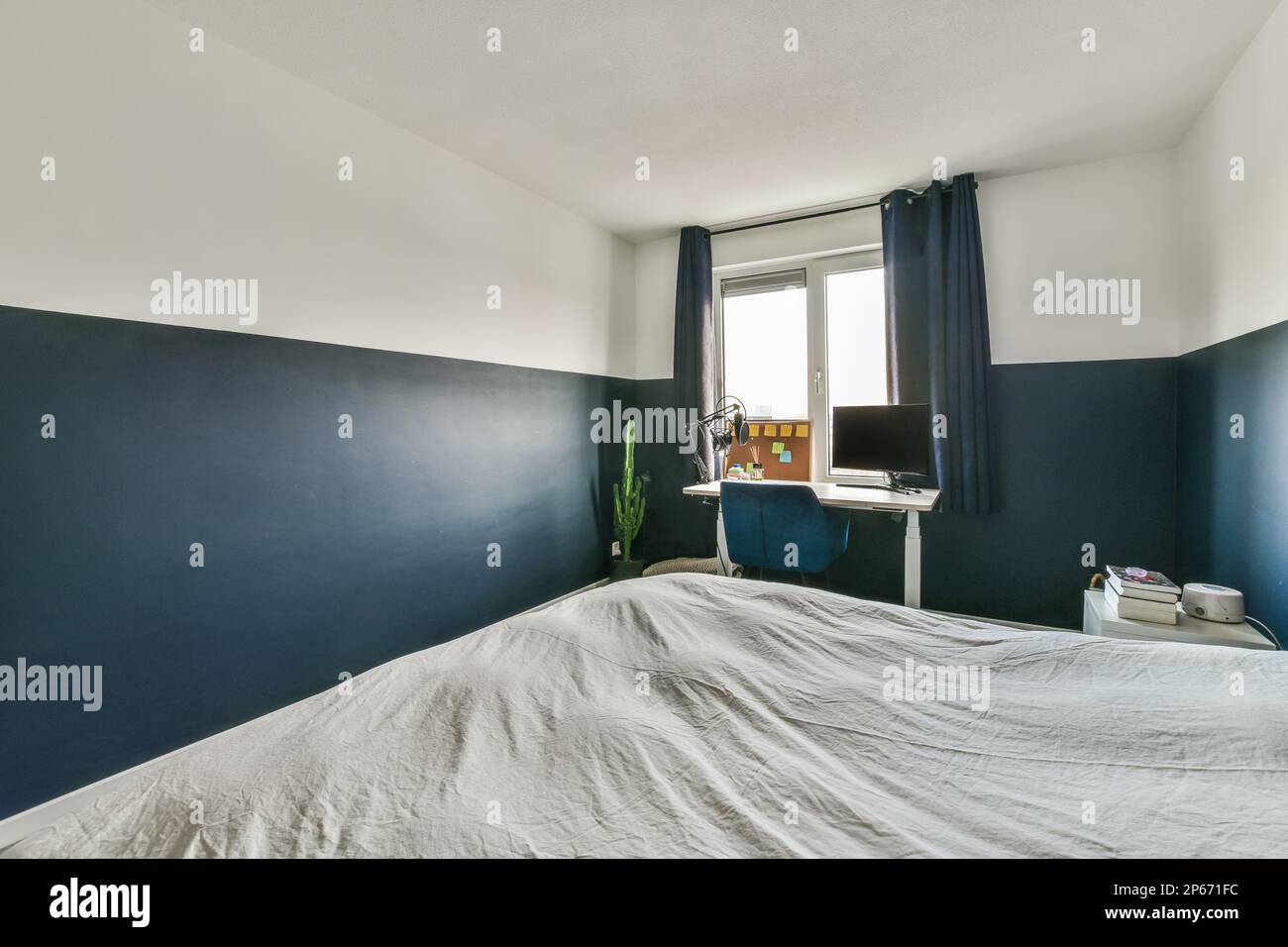 Ein Bett in einem Zimmer mit blauen Wänden und weißen Laken auf dem Bett ist sichtbar Stockfoto