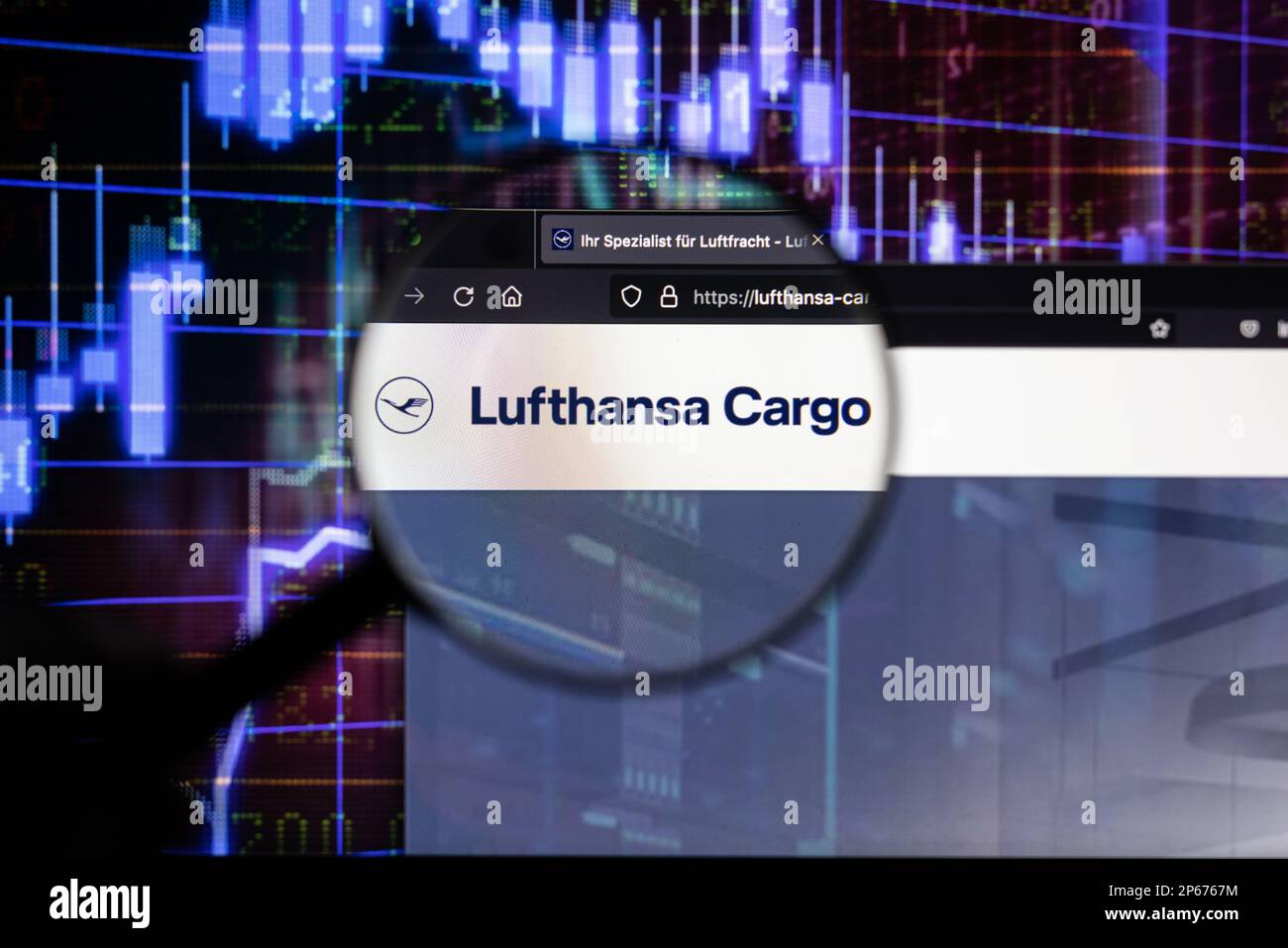 Firmenlogo von Lufthansa Cargo auf einer Website mit verschwommenen Entwicklungen am Aktienmarkt im Hintergrund, auf einem Bildschirm durch eine Lupe zu sehen Stockfoto