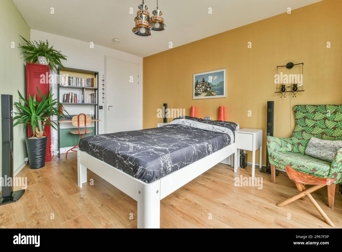Ein Schlafzimmer mit einem Bett, Stuhl und Büchern auf den Regalen vor dem Bett sind gelbe Wände Stockfoto