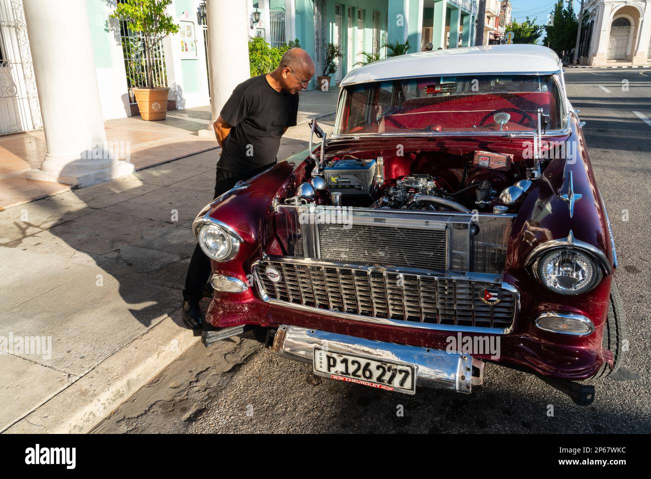 Ein kubanischer Mann inspiziert und bewundert den offenen Motor eines roten klassischen Chevrolet-Autos, Cienfuegos, Kuba, Westindischen, Karibik, Mittelamerika Stockfoto