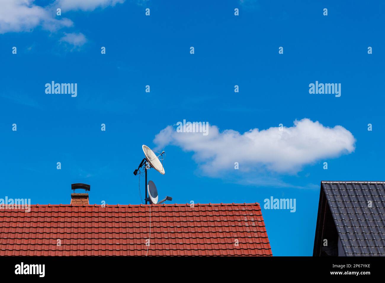 Satellitenschüsseln auf einem gefliesten Dach eines Wohngebäudes. Blauer Himmel mit hellen Wolken. Stockfoto