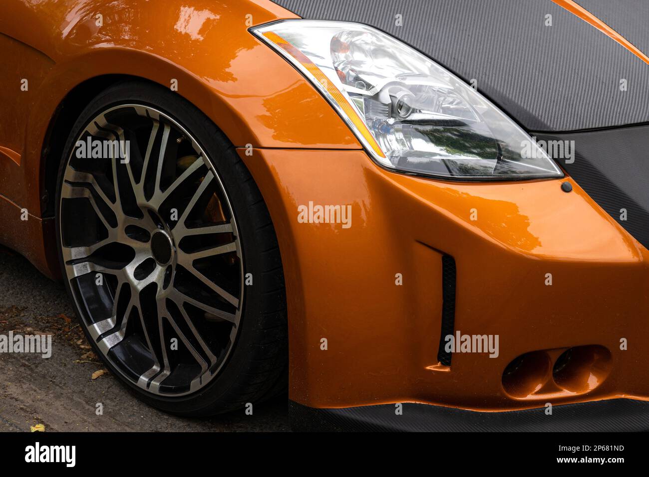 Fragment der Vorderseite eines orangefarbenen Rennwagens. Sichtbarer Scheinwerfer und Rad. Stockfoto