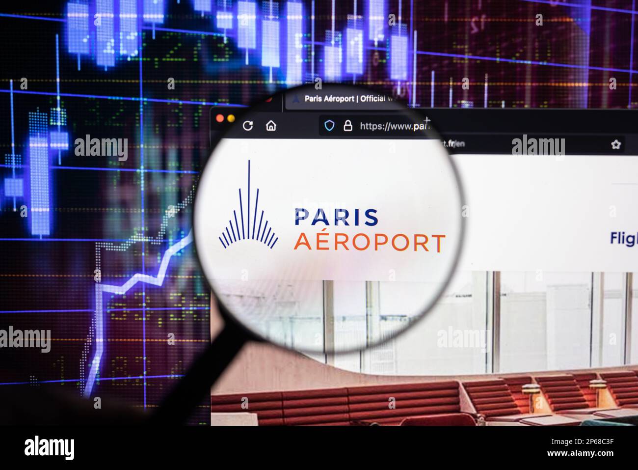 Firmenlogo des Flughafens Paris auf einer Website mit verschwommenen Aktienmarktentwicklungen im Hintergrund, auf einem Computerbildschirm durch eine Lupe zu sehen Stockfoto