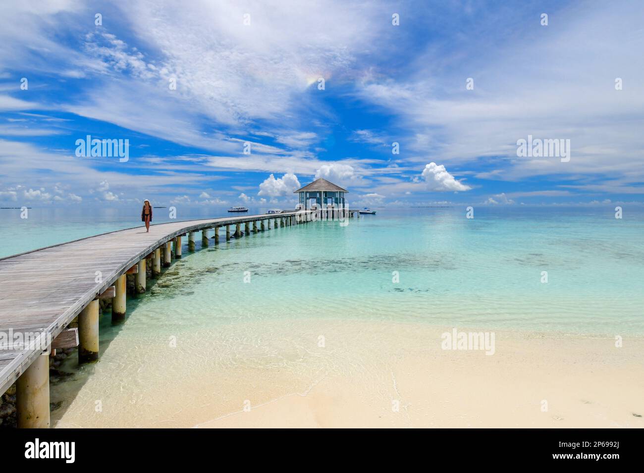 Eine Frau, die auf dem Holzsteg eines Resorts, den Malediven, spaziert Stockfoto