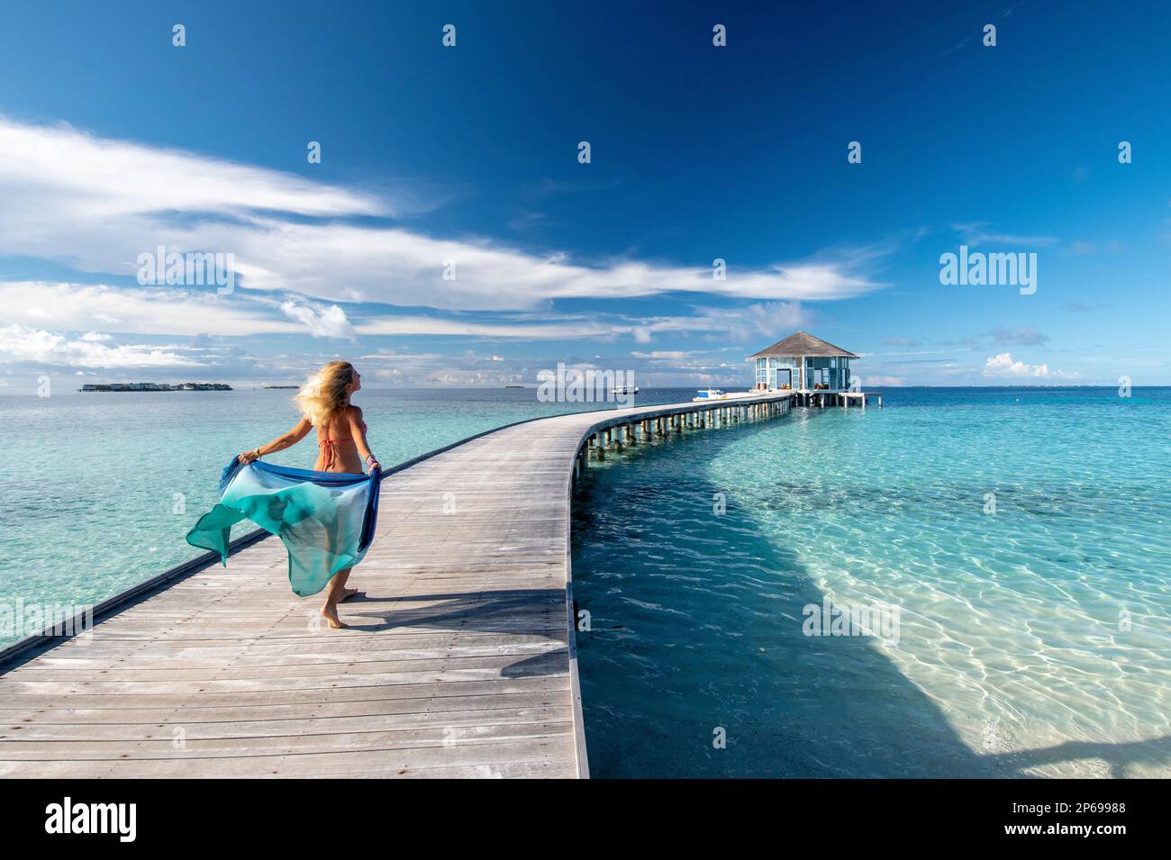 Junge Frau mit einem Sarong, der auf dem hölzernen Steg eines Malediven-Resorts spaziert Stockfoto
