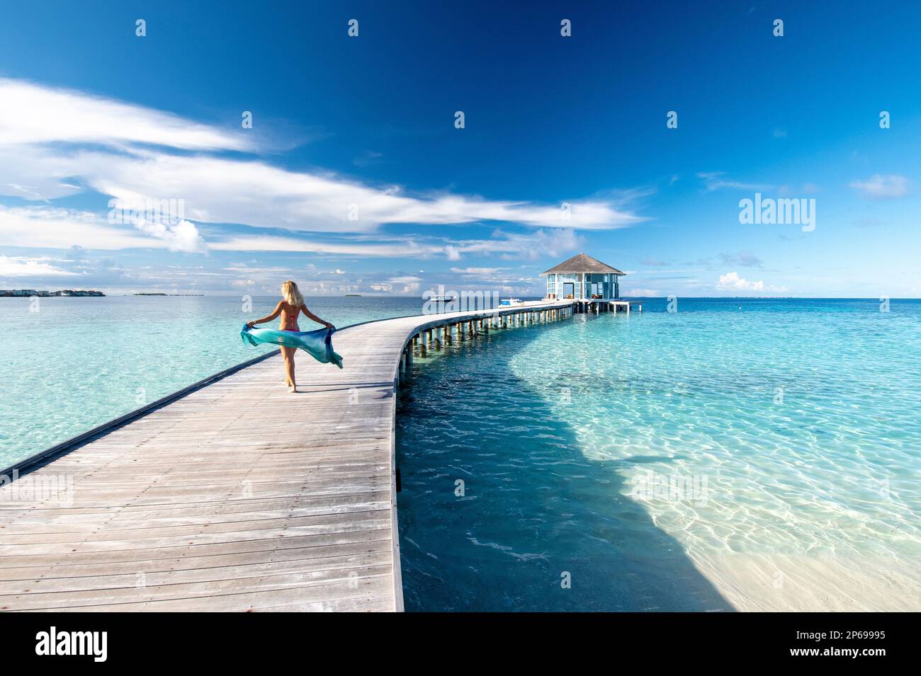 Junge Frau mit einem Sarong, der auf dem hölzernen Steg eines Malediven-Resorts spaziert Stockfoto