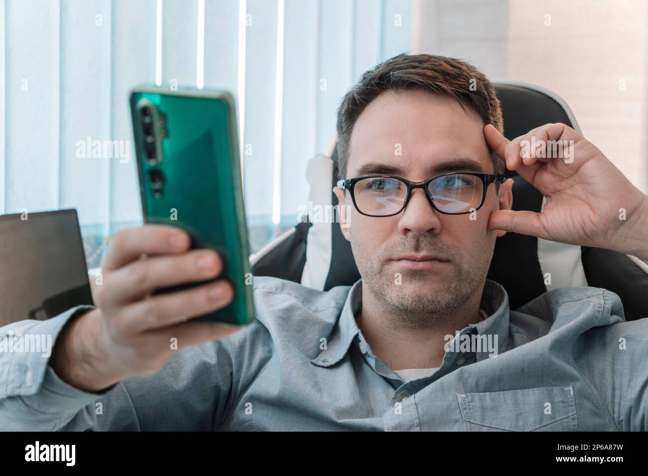 Männchen benutzen moderne Handygeräte, Texten oder Messaging über WLAN. Ein weißer Mann mit Brille sitzt am Schreibtisch im Heimbüro. Schauen Sie sich das Smartphone sc an Stockfoto