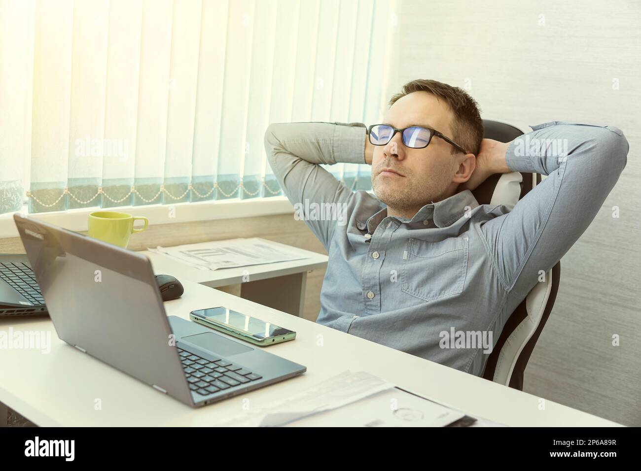 Fröhlich entspannt junger weißer Mann, der sich im Stuhl ruht, abgelenkt von der Computerarbeit, lindert negative Emotionen. Ein ruhiger Mann der Millennials mit Brille, in dem man sich entspannen kann Stockfoto