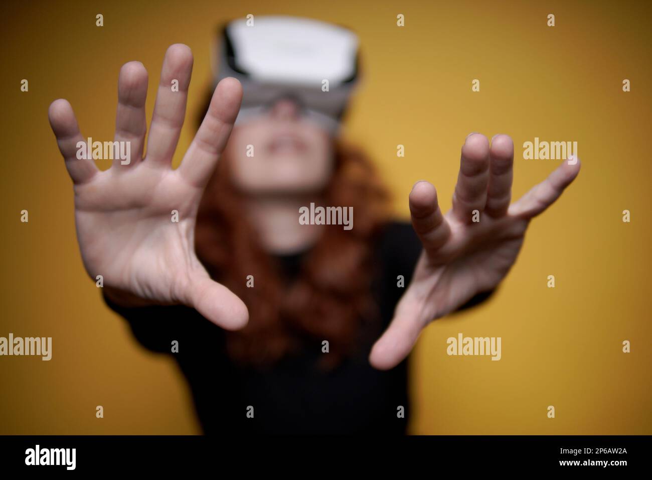 Eine Frau mit einer Virtual-Reality-Brille auf gelbem Hintergrund und den Händen im Vordergrund Stockfoto