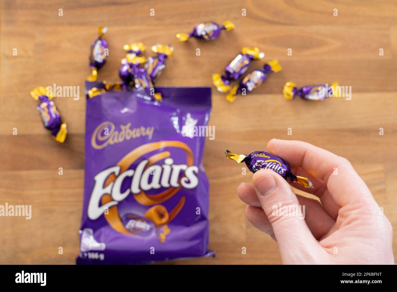 Die Hand eines Mannes, der einen Cadbury-Schokoladen-eclair-Süßstoff hält. UK. Konzept: Cadbury-Marke, ungesunde Ernährung, Snack, Lebensmittelsucht Stockfoto