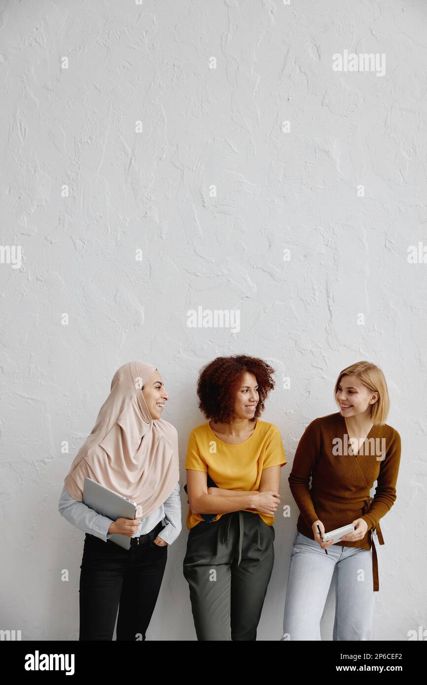 Drei elegante, lächelnde junge Frauen mit unterschiedlicher ethnischer Herkunft, die auf weißem Hintergrund stehen. Stockfoto