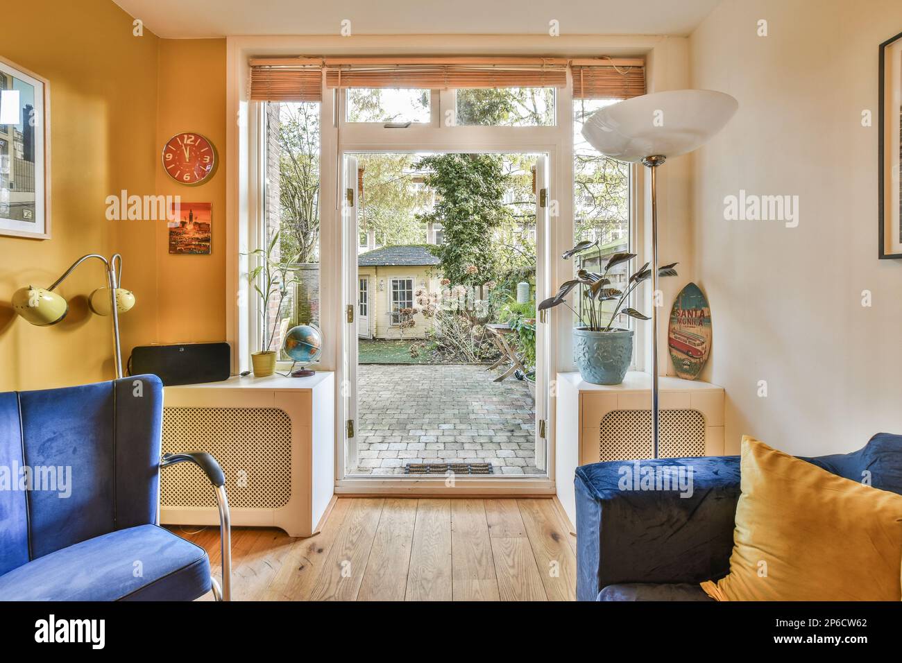 Ein Wohnzimmer mit gelben Wänden und blauen Sofas, eine offene Tür zum Garten im Hintergrund Stockfoto